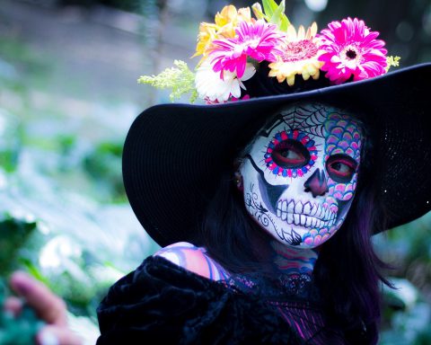 Person painted like a skeleton, wearing a hat decorated with flowers