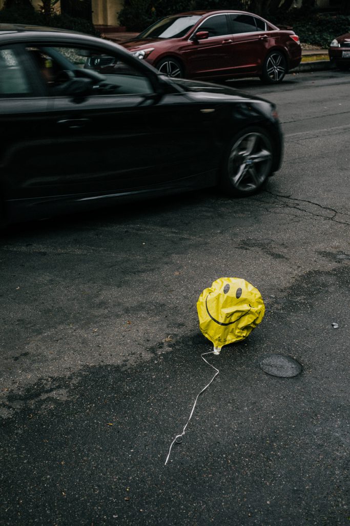yellow smiley balloon, deflated and on the street