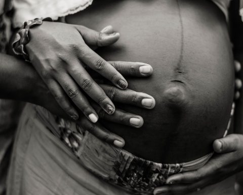 one hand atop another atop a protruding and uncovered pregnant belly