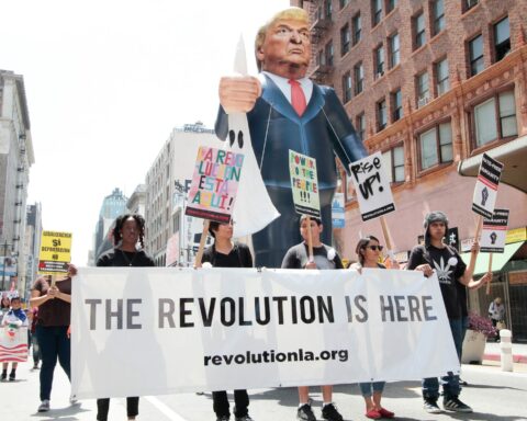 protestors walk with banner and Trump puppet