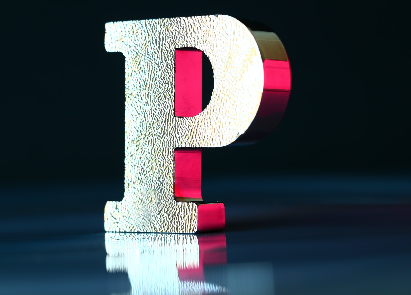 a sculpture of the letter p on a mirrored surface and under a red light