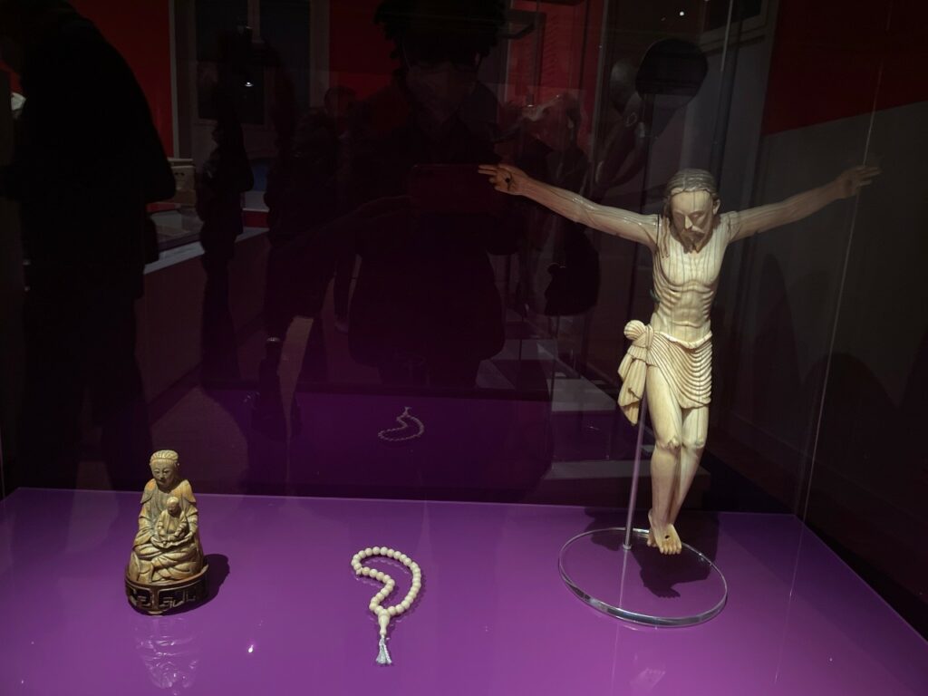 Sculpture of Chinese goddess next to Islamic prayer beads and a Christian crucifix from Sri Lanka, Terrible Beauty, Humboldt Forum